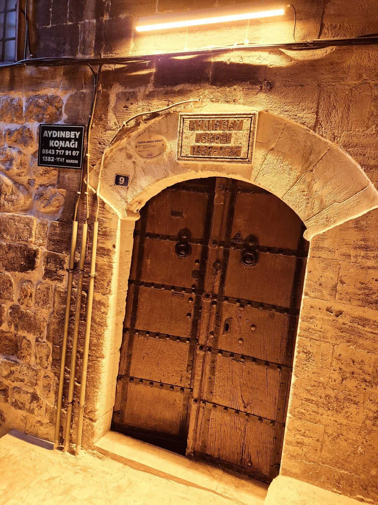A stone building with a large wooden door, a sign with contact information, and a number '9' above the door.