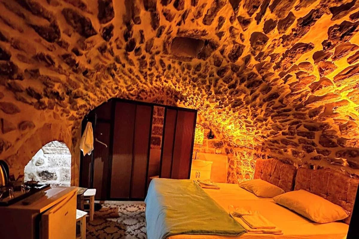 A cozy room with a stone ceiling, a bed with a green blanket, a wooden desk, and a chair.