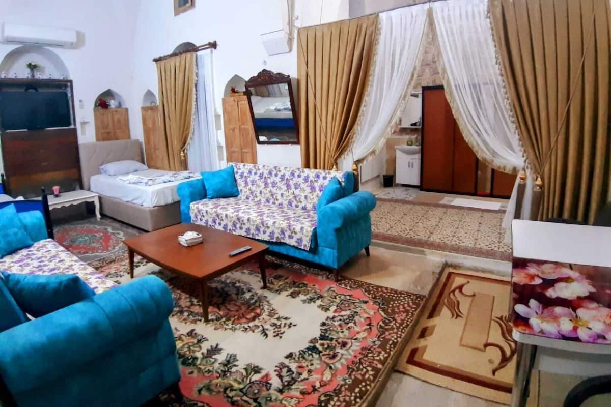 A room with a bed, a sofa, a coffee table, and a TV. There are curtains and a window.