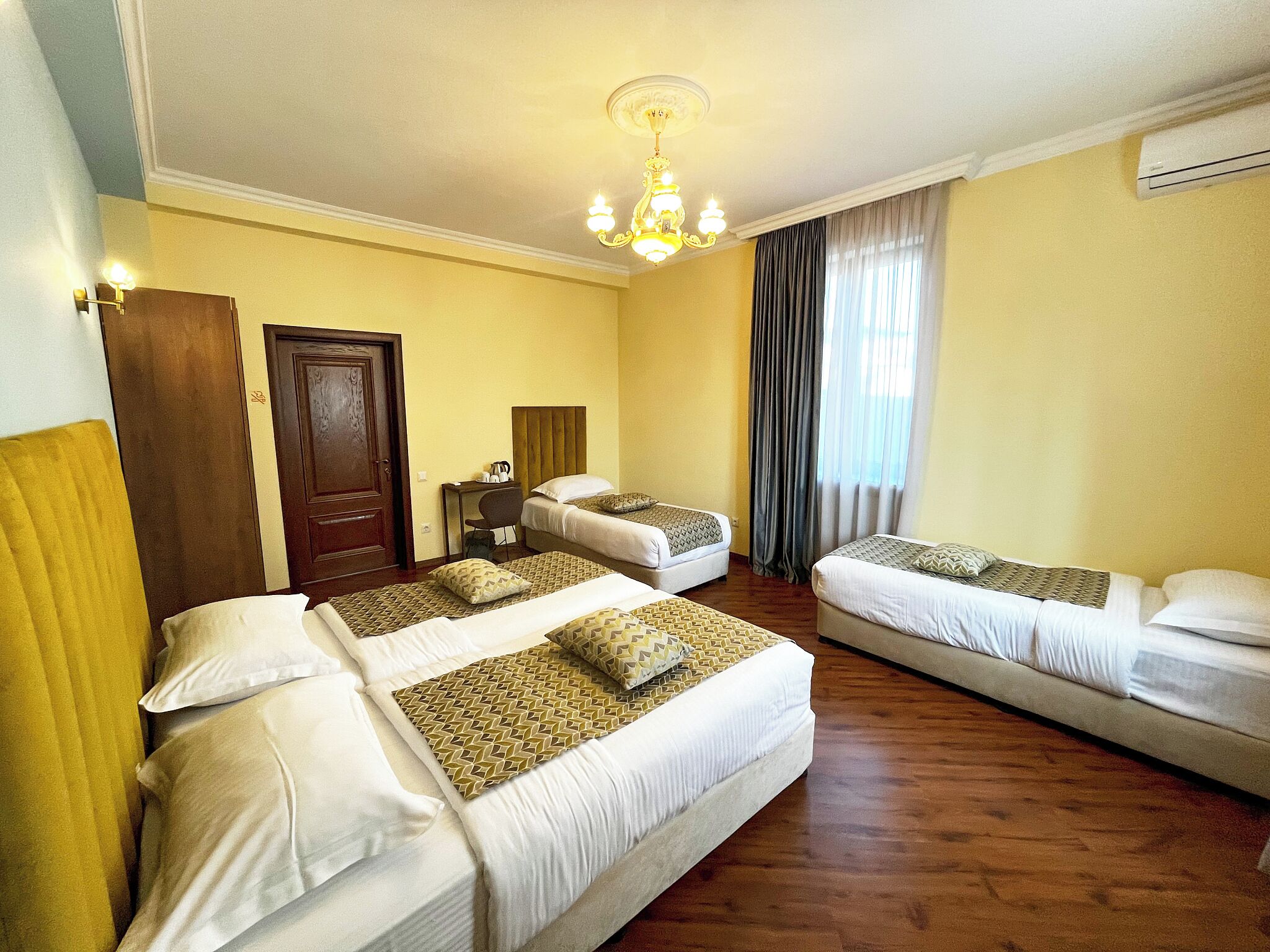 Habitación de hotel con dos camas individuales, una cama doble, un escritorio con silla, una araña y una puerta.
