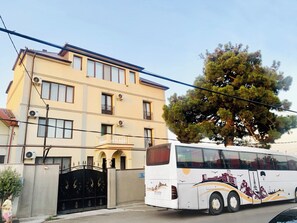 Un edificio de varios pisos con un balcón, un árbol grande en la parte delantera y un autobús estacionado.
