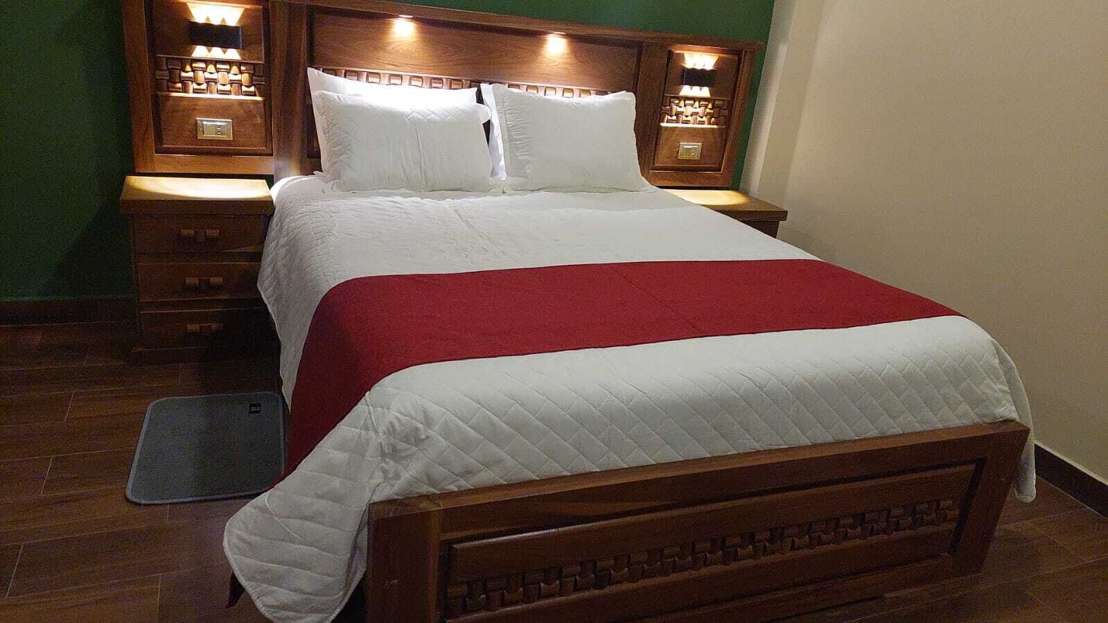 A neatly made bed with a red and white bedspread, wooden headboard, and bedside lamps.