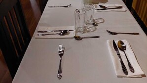 Una mesa de comedor dispuesta con cubiertos y vasos, rodeada de sillas de madera.