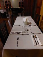 Una mesa de comedor dispuesta con cubiertos y vasos, rodeada de sillas de madera.