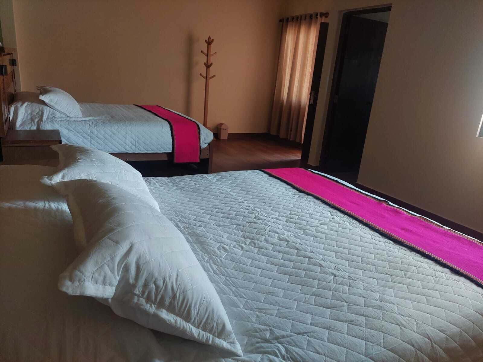 A hotel room with two beds, a wooden coat rack, and a door with curtains.