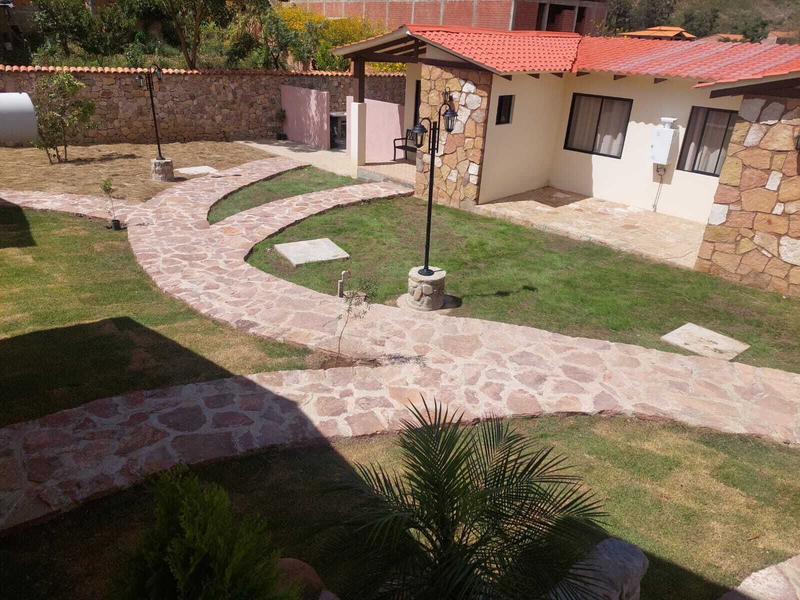 A stone pathway leading to a covered patio area with a stone wall and a small building with a red-tiled roof.