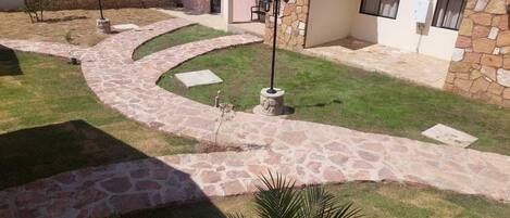 A stone pathway leading to a covered patio area with a stone wall and a small building with a red-tiled roof.