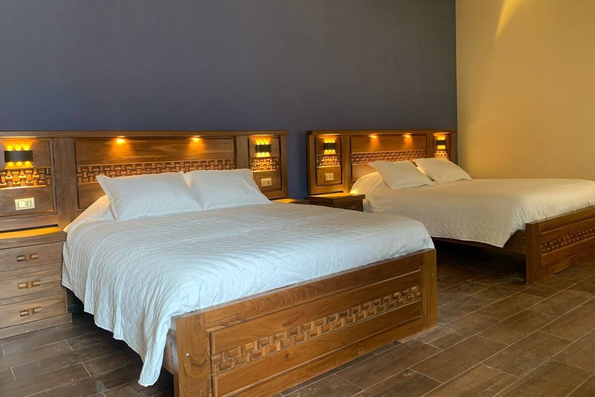 Habitación de hotel con dos camas de madera, cada una con cabecero de diseño geométrico e iluminación integrada.