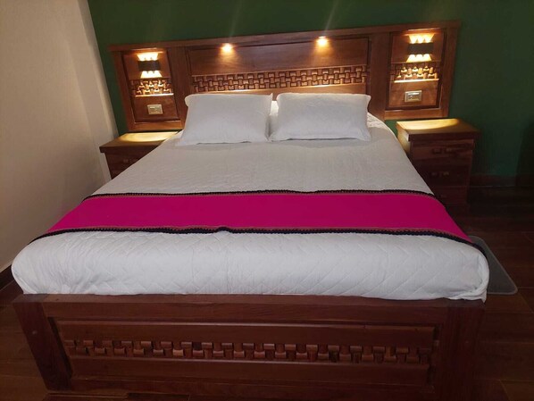 A bed with a wooden headboard, two bedside tables, and a bright wall.