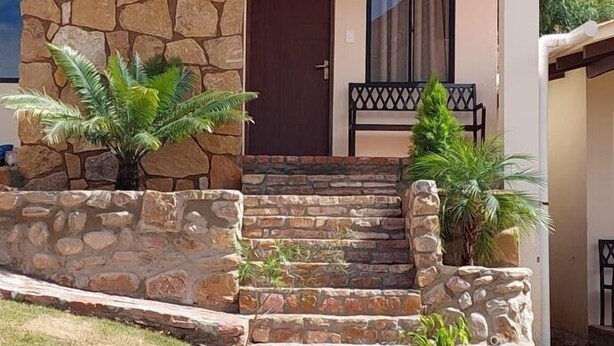 Una casa de dos pisos con fachada de piedra, una puerta marrón y un pequeño porche con escalones que conducen a la entrada.