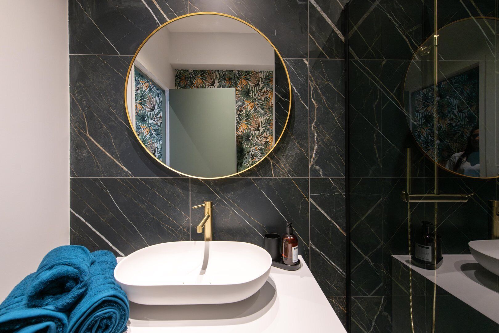Une salle de bain moderne avec un grand miroir ovale, un robinet doré et un lavabo blanc.