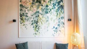 A room with a wooden ceiling, a white sofa with two green pillows, a large floral artwork on the wall, and a floor lamp. - Lassagne - 2 - New studio in the city center (Lyon)