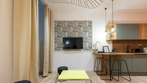 Une cuisine moderne avec un plan de travail en bois, des tabourets de bar et un téléviseur fixé au mur.
