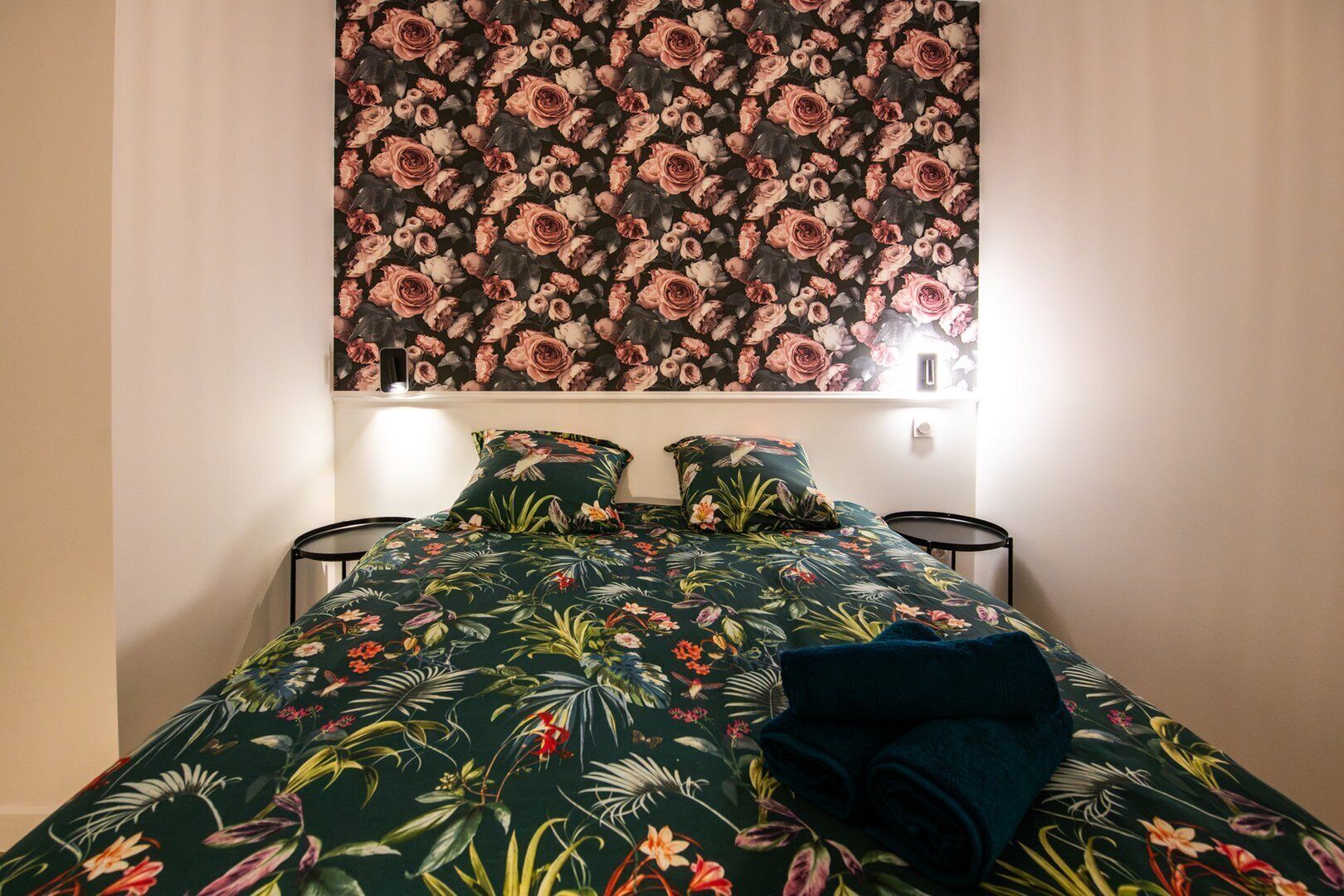 A bedroom with a floral-patterned bedspread, two matching pillows, and a dark blue blanket.