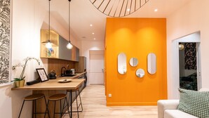 Une cuisine moderne avec un plan de travail en bois, des tabourets de bar et des luminaires suspendus. On y trouve également un coin repas avec un canapé et un mur décoré de miroirs.