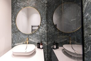 Une salle de bain moderne avec deux lavabos, des murs en marbre et de grands miroirs.