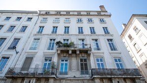 Un immeuble à plusieurs étages de style architectural classique, doté d’un balcon central orné de colonnes et d’une rangée de fenêtres à chaque étage.