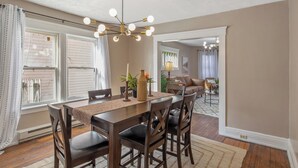 A dining area with a wooden table, dark chairs, a chandelier, and a view into another room with a sofa and a lamp. - Downtown Syracuse 2BR Near University & Zoo (Syracuse)
