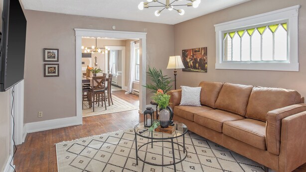 A living room with a brown leather sofa, a glass coffee table, and a chandelier. There is a dining area visible through an open door. - Downtown Syracuse 2BR Near University & Zoo (Syracuse)
