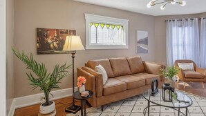 A living room with a brown leather sofa, a glass coffee table, a floor lamp, a potted plant, and a painting on the wall. - Downtown Syracuse 2BR Near University & Zoo (Syracuse)