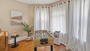 A room with a foosball table, a sofa, a small table with a flower, and a potted plant. - Downtown Syracuse 2BR Near University & Zoo (Syracuse)