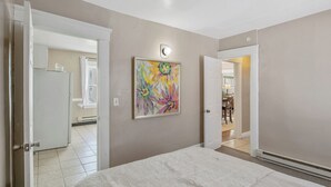 A bedroom with a bed, a door leading to a bathroom, and a hallway with a light fixture. - Downtown Syracuse 2BR Near University & Zoo (Syracuse)