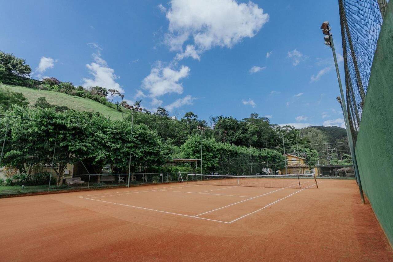 Een tennisbaan buiten met een net, omringd door bomen en een heldere lucht.