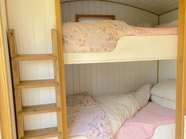 A bunk bed with a wooden ladder, a window above, and a wall with vertical paneling.
