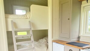 En køjeseng med stige, et lille køleskab og et træskrivebord med tastatur.