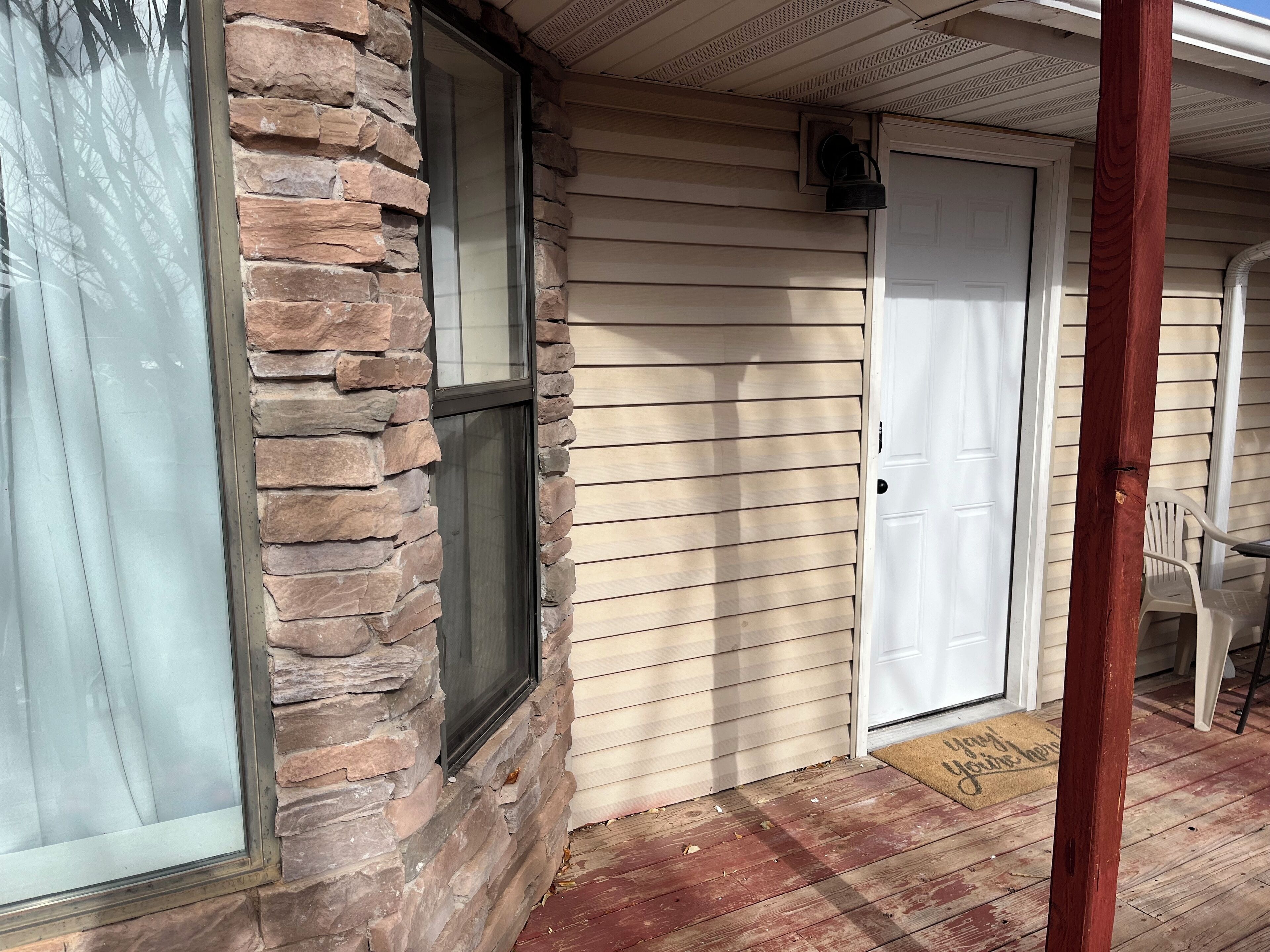 A house with a stone exterior, a wooden door, and a porch with a chair.