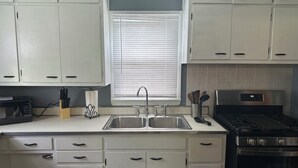 A kitchen with white cabinets, a stainless steel sink, a stove, and a window with blinds. - Charming 2-bedroom house in brilliant Indianapolis with AC, WiFi (Indianapolis)