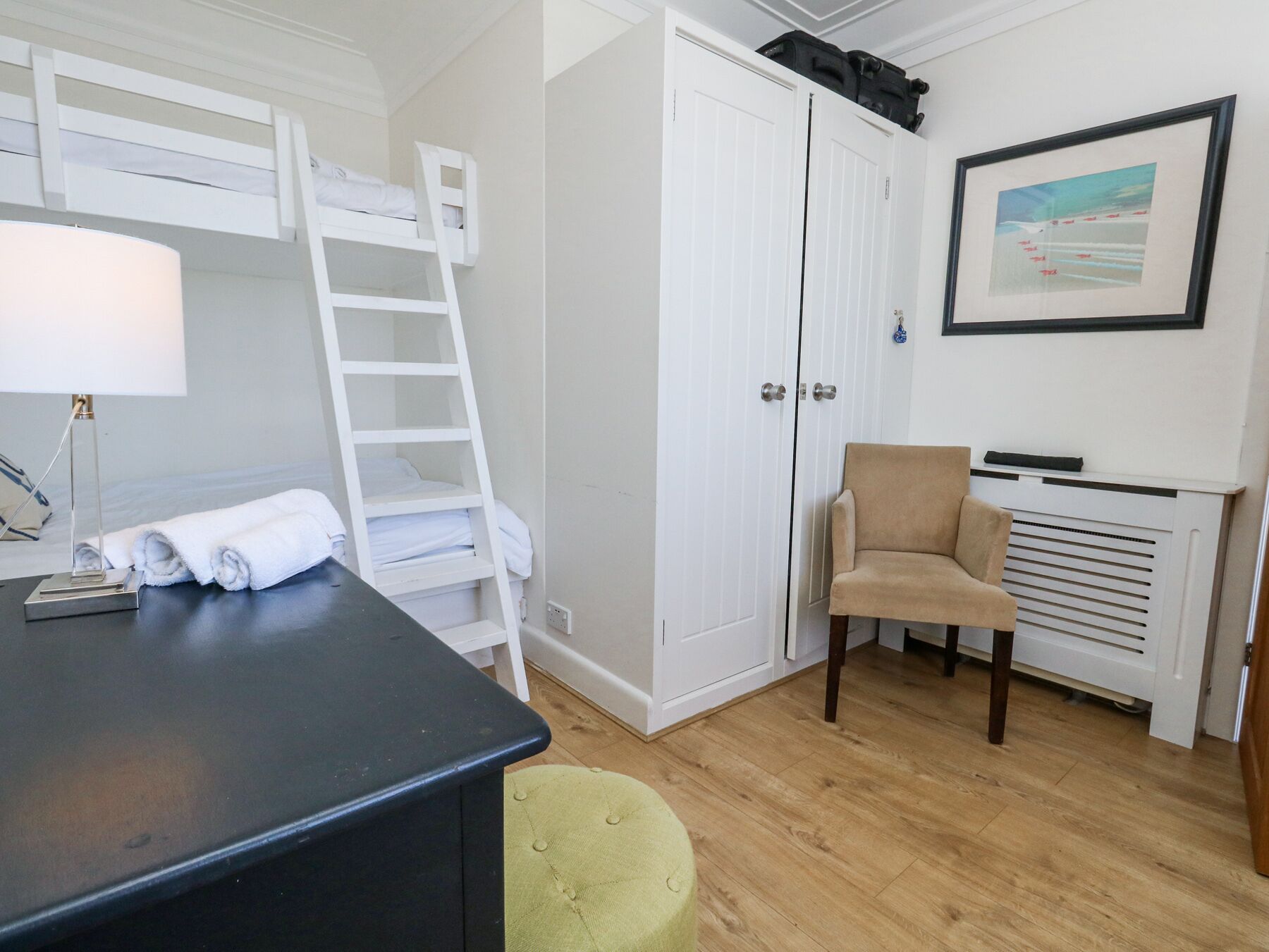 A room with a bunk bed, a desk with a lamp, a chair, and a radiator.