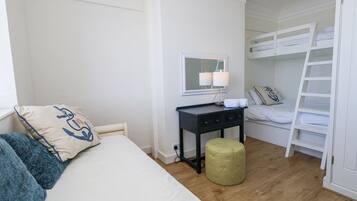 Et soveværelse med en seng, et skrivebord, et spejl, en køjeseng og en grøn puf.