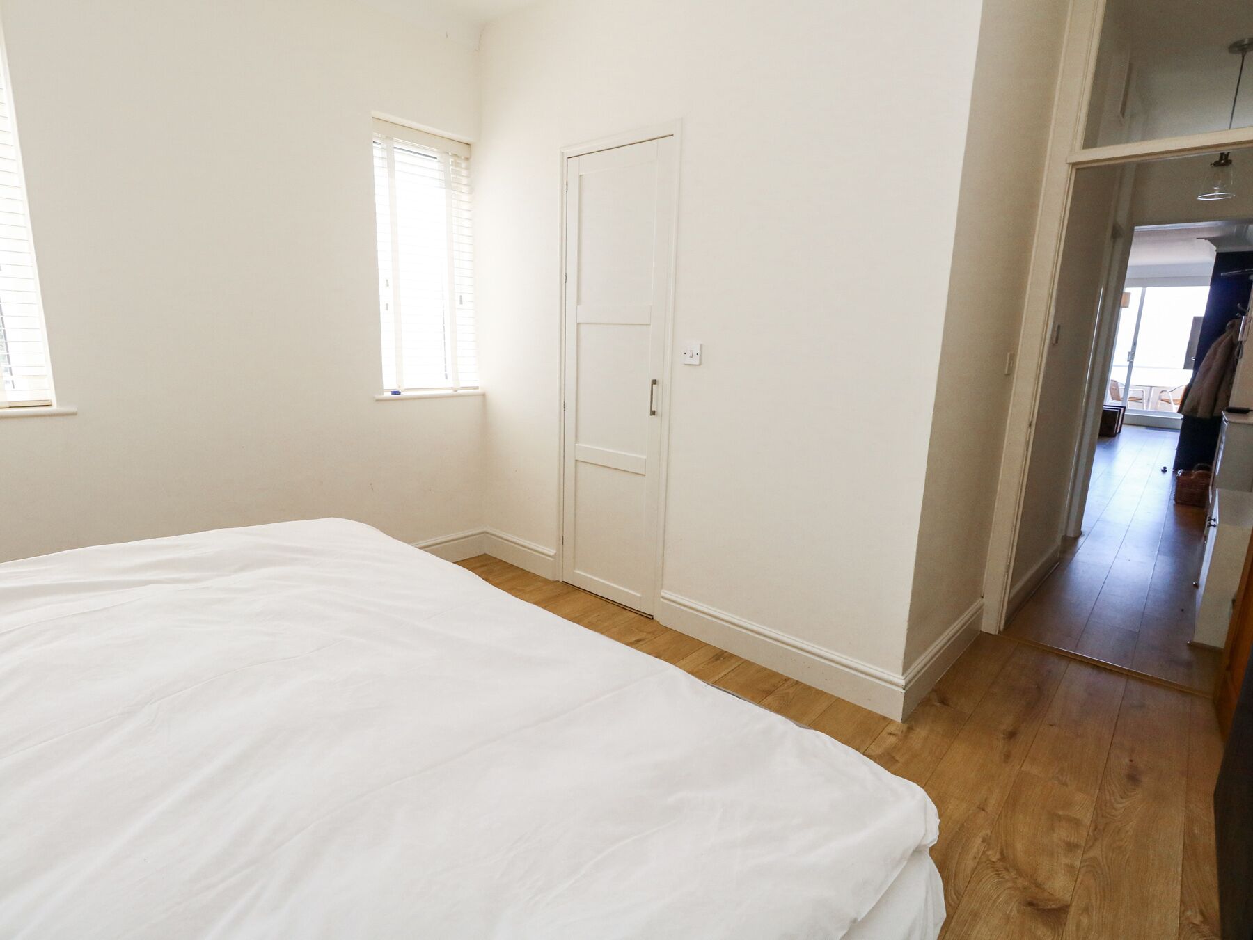 A bedroom with a large bed, a window, and a door leading to another room.
