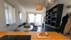 A modern kitchen with a wooden countertop, a dining area with a table and chairs, and a view of the living room. - Flat 7 Sand Acres (Poole)