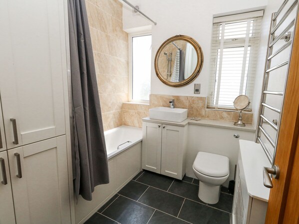 A bathroom with a bathtub, a toilet, a sink, and a mirror. - Flat 7 Sand Acres (Poole)