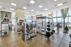 Ein Fitnessstudio mit verschiedenen Trainingsgeräten, großen Fenstern und Blick auf die Stadt.