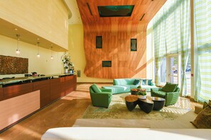 Eine moderne Hotelhalle mit Holzbalkendecke, grünen Sofas, einer Rezeption und großen Fenstern.