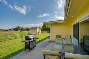 Eine überdachte Terrasse mit Grill, Gartenmöbeln und Blick auf ein grünes Feld.