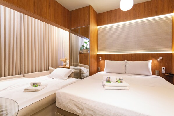 A hotel room with two beds, wooden paneling, a large mirror, and a bedside table with a lamp.