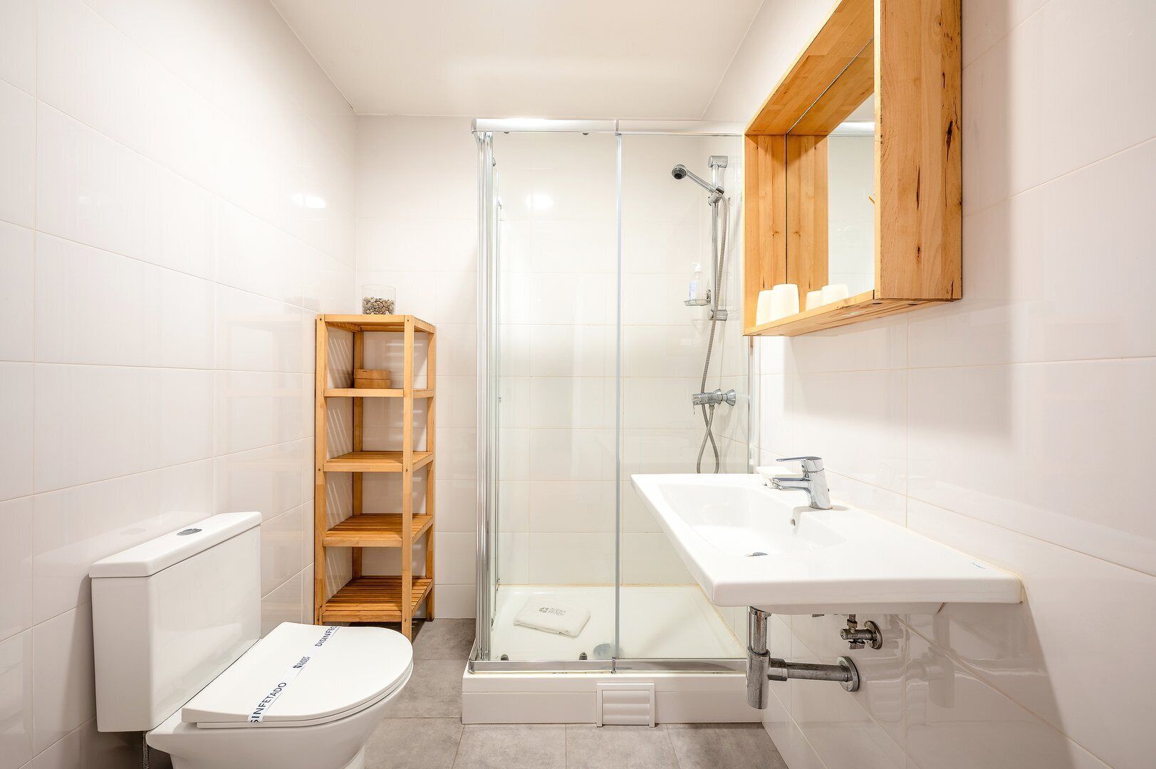Een moderne badkamer met een glazen douchecabine, een houten plank, een wit toilet en een wastafel met een houten kast erboven.