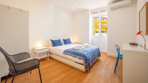 Een slaapkamer met een bed, nachtkastjes, een stoel, een bureau en een airconditioning.