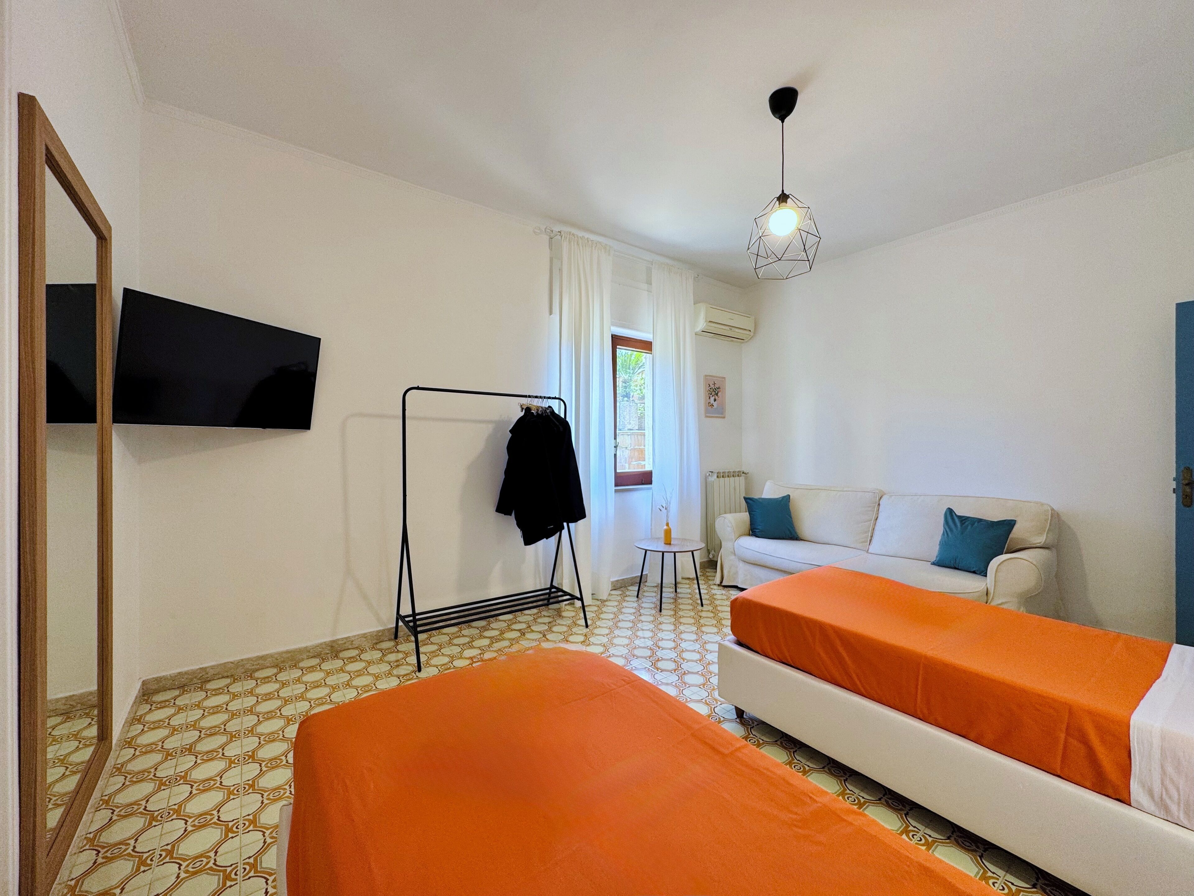 Hotelkamer met twee bedden, een slaapbank, een televisie, een kapstok en een raam met gordijnen.