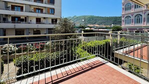 Un immeuble à plusieurs étages doté de balcons, une cour intérieure agrémentée de plantes et une vue sur un paysage vallonné.