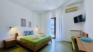 Une chambre d’hôtel avec un lit, un bureau, une chaise, une télévision et une fenêtre avec des rideaux.