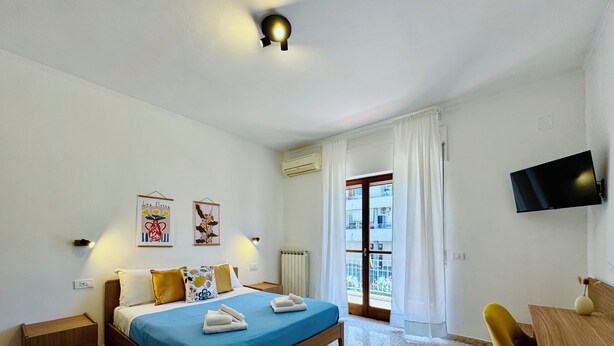 Une chambre d’hôtel avec un lit, un bureau, une chaise, une télévision et une fenêtre avec des rideaux.
