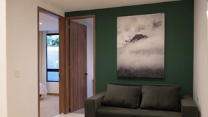 A modern living room with a dark green accent wall, a large painting of a mountain landscape, and a dark grey sofa with cushions. - Deluxe queen suite (Salento)