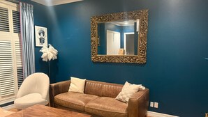 Un salon avec un canapé en cuir marron, un fauteuil blanc et une table basse en bois. Un grand miroir décoratif est accroché au mur.