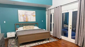 Une chambre à coucher comprenant un lit, une table de chevet, une commode, une fenêtre avec des rideaux et une porte donnant sur un balcon.