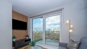 A modern living room with a large window, a flat-screen TV, and a minimalist design. - Luxury Waterfront 2BR - Free Gym Access & Parking (Stretford)